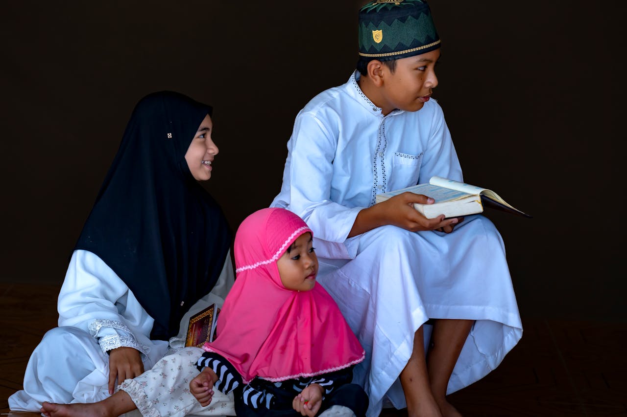services-01 Three children reading the Quran together, wearing traditional outfits.